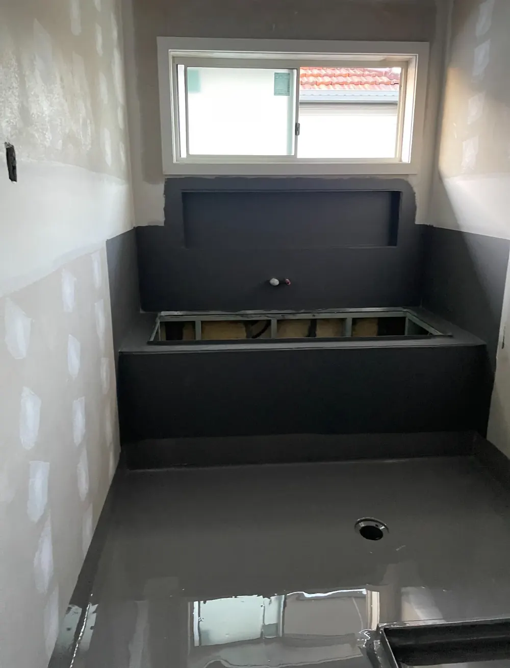 Bathroom with a bath hob and floor in dark grey membrane, window above
