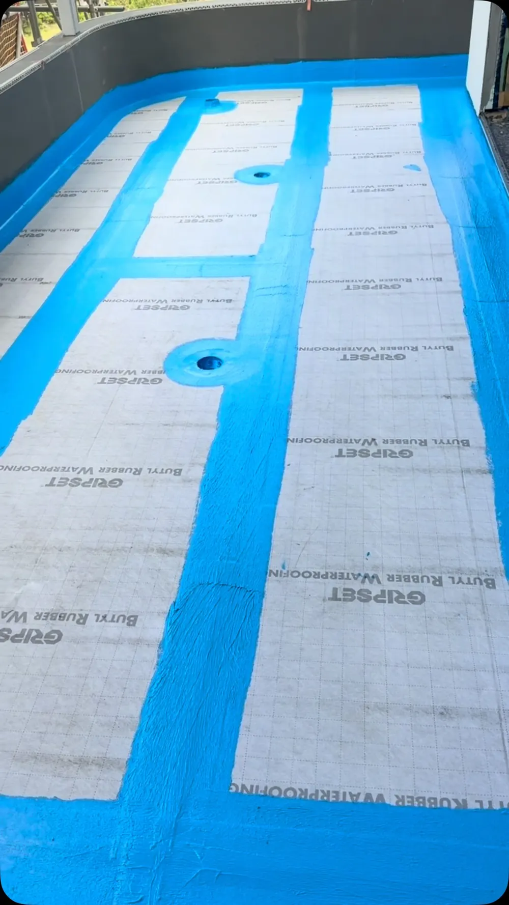 Balcony laid with grey Gripset butyl rubber sheet membrane, every joint, edge and floor waste coated in blue