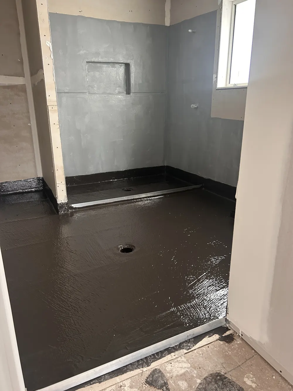 Shower recess and bathroom floor in dark grey membrane with a niche in the wall